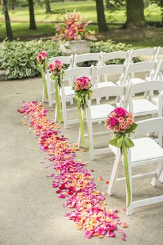 the aisle is lined with white chairs and pink flowers