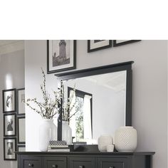 a black dresser and mirror in a room with pictures on the wall above it, along with vases filled with flowers