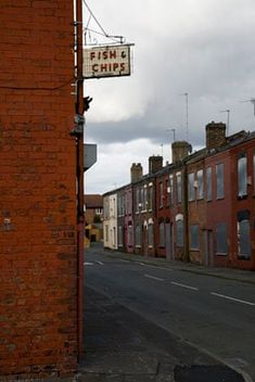 an old brick building on the side of a road with a sign hanging off it's side