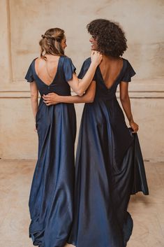 two women in dresses standing next to each other and looking at each other with their backs turned