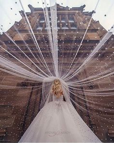 a woman in a wedding dress is standing with her veil over her head and looking up at the sky