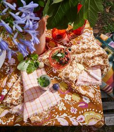 a table topped with plates and bowls filled with food next to purple flowers on top of a wooden bench