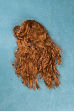 a long red curly wig laying on top of a blue surface