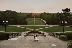 a bride and groom standing in front of a large lawn area at sunset with the sun setting behind them