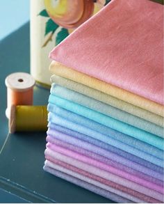 a stack of different colored cloths next to a spool of thread on a table