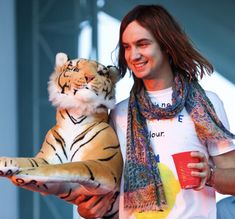 a man holding a stuffed tiger in his right hand and wearing a scarf around his neck