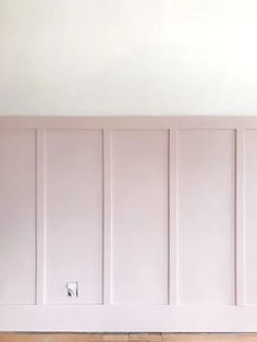 an empty room with white paneling and wood flooring on the walls, painted in pale pink