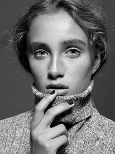 a black and white photo of a woman with her hand on her chin, looking at the camera