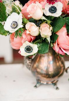 a silver vase filled with lots of flowers on top of a white tablecloth covered table