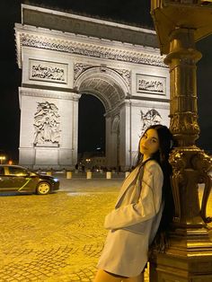 a woman leaning against a pole in front of the arc de trio triumph at night