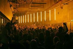 a large group of people in a room with lights on the ceiling and some are holding up their hands