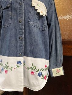 a blue jean jacket with white and pink flowers on the front, hanging from a wooden hanger