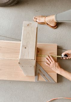 a woman is working on some wood with a pair of scissors and a tape measure