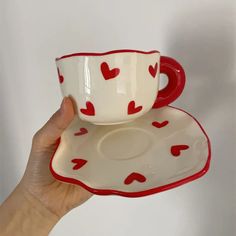 a hand holding a cup and saucer with hearts on it