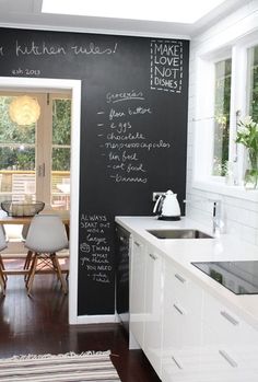 a chalkboard wall in a kitchen with white cabinets and wooden flooring is painted black