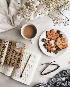 a cup of coffee and some cookies on a table next to an open book with glasses