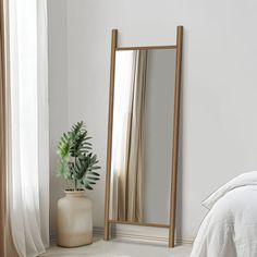 a large mirror sitting on top of a white floor next to a plant in a vase