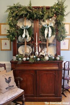 an old china cabinet decorated for christmas with greenery and silver ornaments