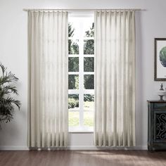 an open window with white curtains and wooden flooring in front of a potted plant