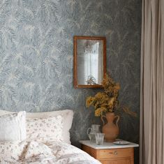 a bedroom with blue wallpaper and white bedding, vase with flowers on the nightstand