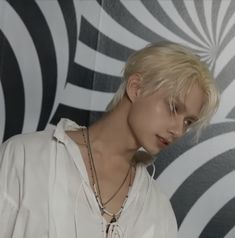 a woman with blonde hair wearing a white shirt and silver necklace standing in front of a black and white wall