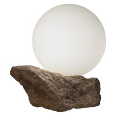 a white ball sitting on top of a rock next to a large stone object with a light inside it