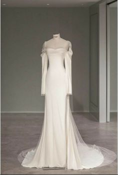 a white wedding dress with long sleeves on display in front of a wall and floor