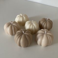 five small pumpkins sitting on top of a white table next to each other and one candle in the middle