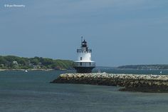 a light house sitting on top of a rock wall next to the ocean with boats in the water