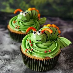 two cupcakes with green frosting and orange decorations on them, sitting on a table