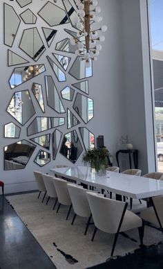 a dining room table with white chairs and mirrors on the wall