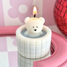 a small white teddy bear sitting inside of a candle holder on a pink and white checkered table