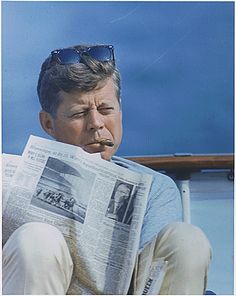 a man sitting down reading a newspaper with sunglasses on his head