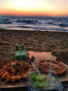 two pizzas and salad on the beach at sunset