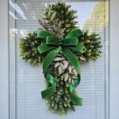 a wreath is hanging on the door with green ribbon and leaves attached to it's front