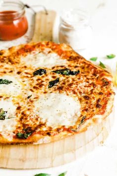 a pizza sitting on top of a wooden cutting board next to sauces and condiments