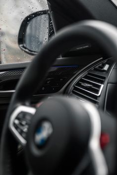 the interior of a car with steering wheel controls and dashboard lights, rain drops on the windshield