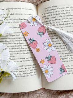 a bookmark with strawberries and daisies is laying on top of an open book