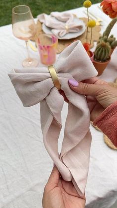 a woman is holding up a pink bow on her napkin at a table with wine glasses and succulents