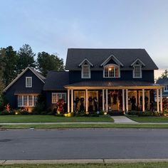 a large blue house with white columns and lights on it's front porch at dusk