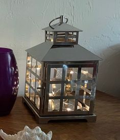 a purple vase sitting on top of a wooden table next to a lit up lantern