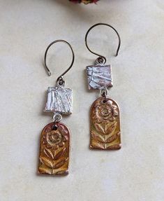 two silver and gold earrings on a white table next to a vase with flowers in it