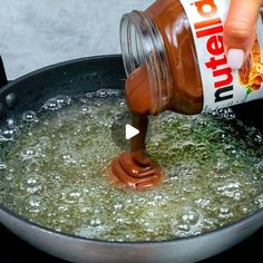 a person pouring peanut butter into a frying pan filled with boiling water and oil