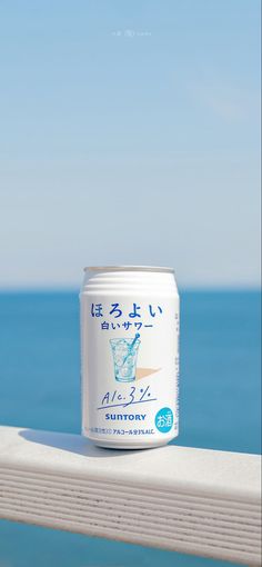 a can of water sitting on top of a white fence next to the ocean with blue sky in the background