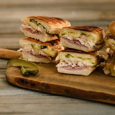 several sandwiches cut in half on a cutting board with pickles next to the sandwich