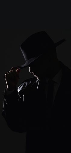 a man in a black suit and hat is holding his hand up to his face