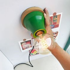 a person is holding a green light bulb in their left hand and there are pictures on the wall behind them