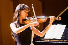 a woman playing the violin in front of a piano with music sheets on it and an instrument behind her