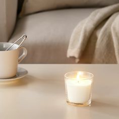 a lit candle sitting on top of a table next to a cup and saucer