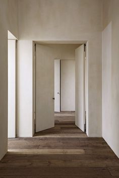 an empty hallway with white walls and wood flooring is seen in this image from the inside